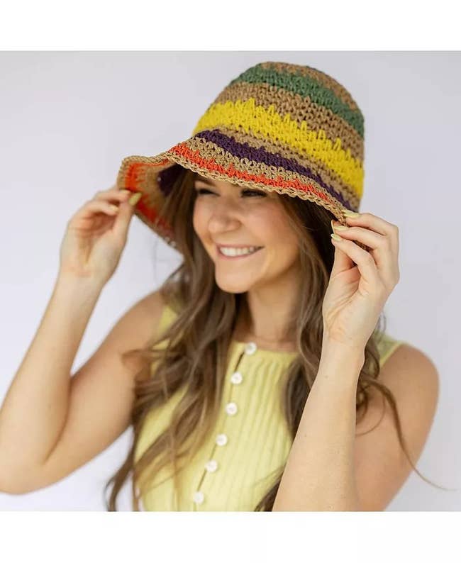 A smiling person wears a striped crochet bucket hat and a sleeveless ribbed dress with buttons, perfect for summer fashion in a shopping feature