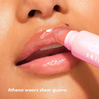 Close-up of lips applying sheer guava lip gloss with a pink applicator. Text reads: