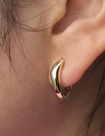 Close-up of an ear wearing a small, sleek, crescent-shaped hoop earring, suitable for elegant or casual styles