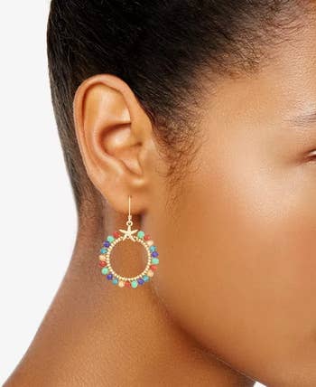 Person wearing a circular earring featuring colorful beads, showcasing a trendy accessory likely highlighted in a shopping article