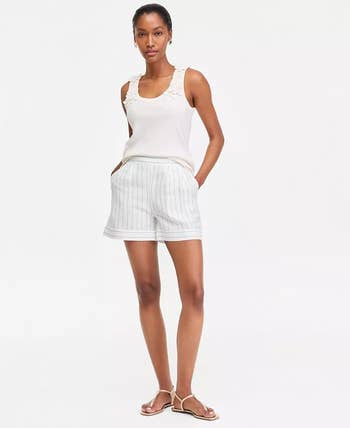 Person wearing a sleeveless top, striped shorts, and sandals, standing against a plain background. Fashionable casual summer attire