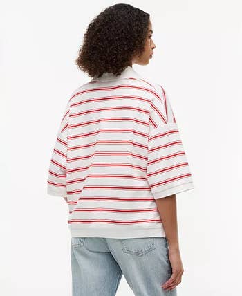 Person wearing a casual, loose-fitting striped top with elbow-length sleeves, paired with light blue jeans, seen from the back