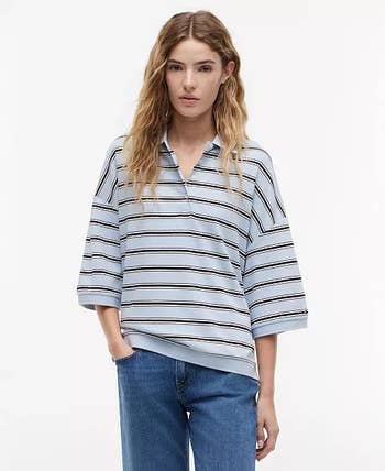 Person wearing a casual striped top with loose sleeves and jeans stands posed, suitable for a relaxed fashion or shopping article