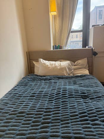 Cozy bedroom with a neatly made bed featuring a textured blanket and fluffy pillows, under soft natural light from a window