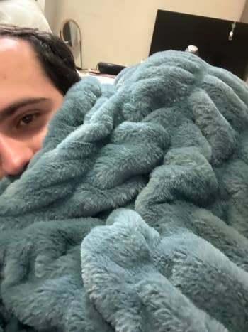 Writer snuggled under a soft, plush blanket indoors, partially showing their face
