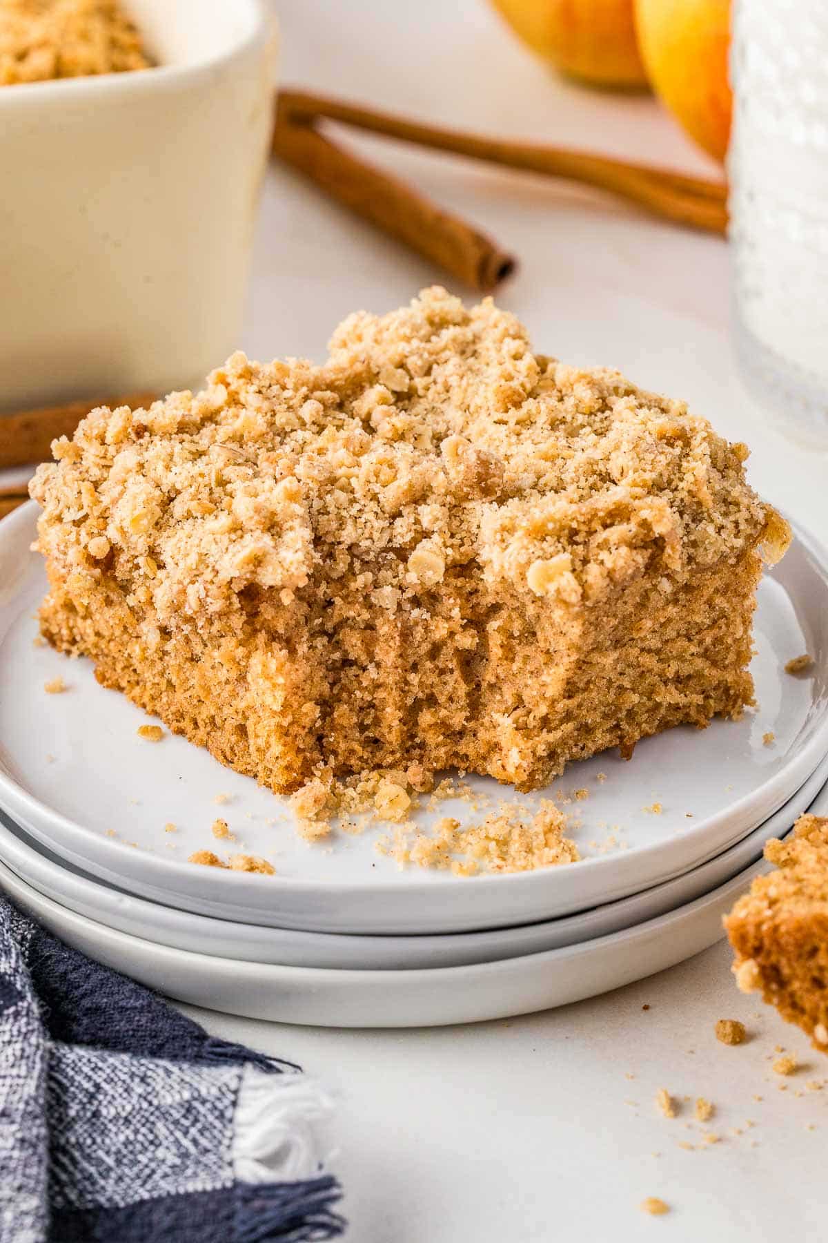 A square piece of Applesauce Crumb Cake sits on stacked white plates with crumbs scattered around.