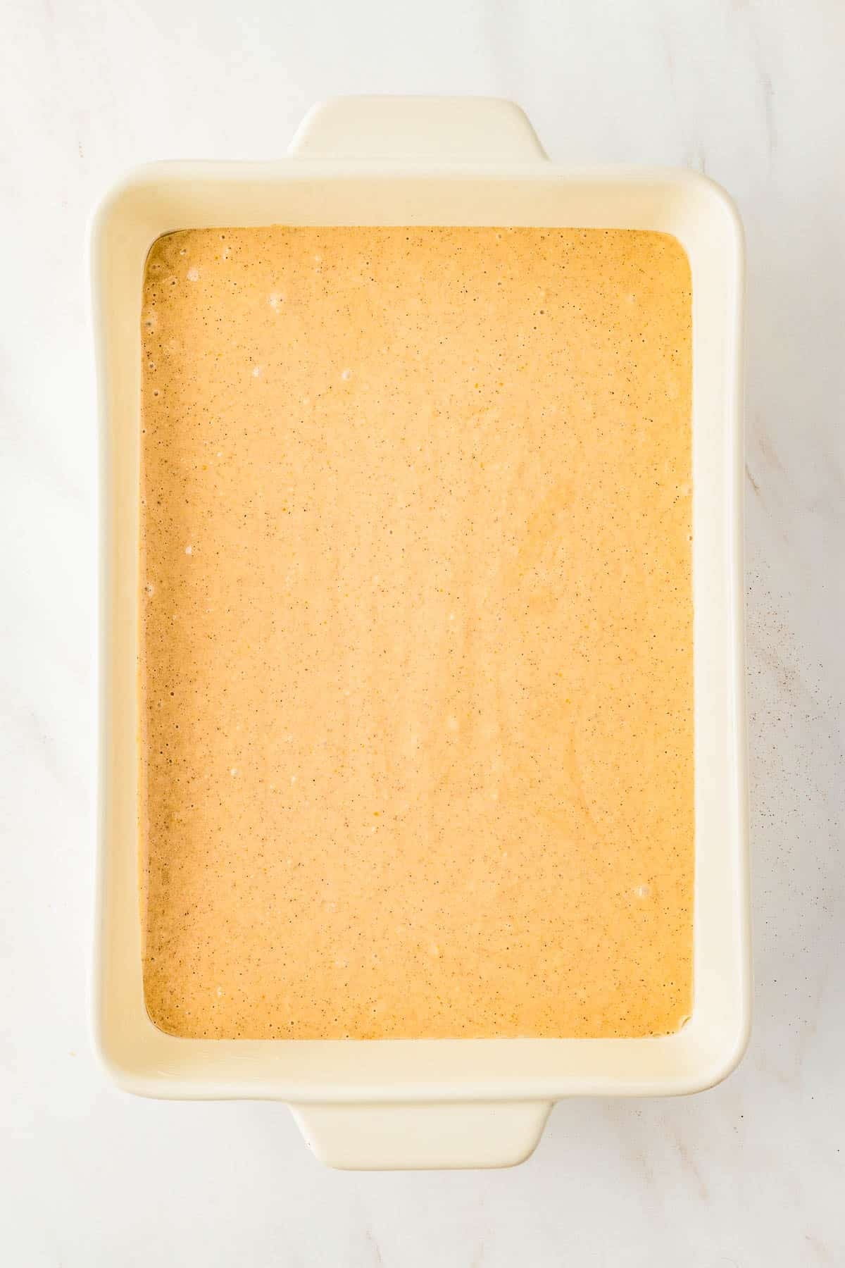 A rectangular white baking dish filled with an even layer of Applesauce Crumb Cake batter.