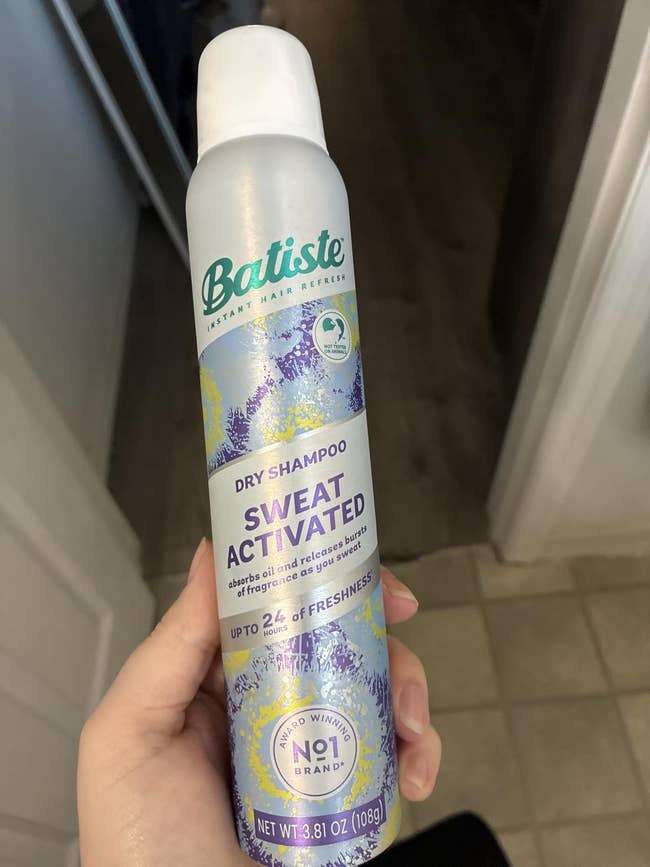 A hand holds a bottle of Batiste Sweat Activated Dry Shampoo