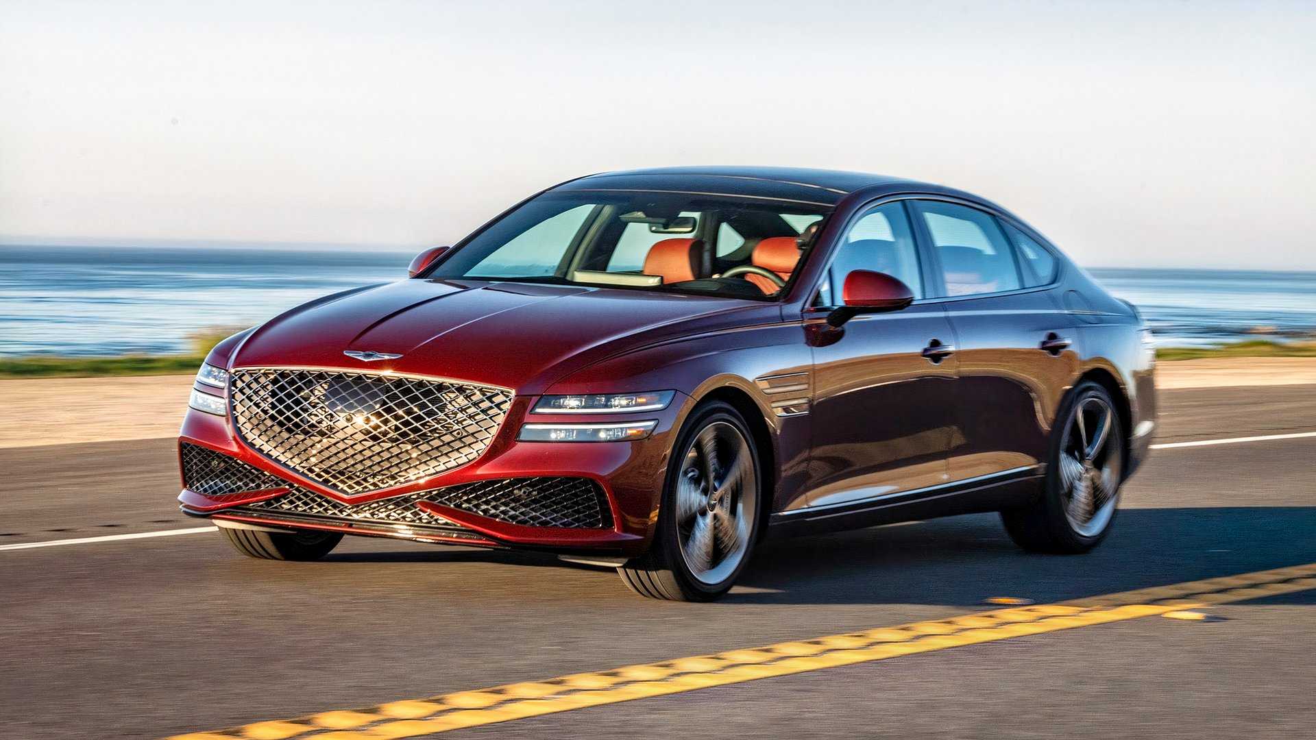 A red 2022 Genesis G80 driving on a coast road shown in front 3/4 view