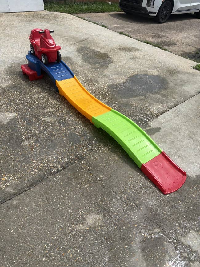 Children's roller coaster toy set up on a driveway, featuring a small red ride-on car on a colorful ramp