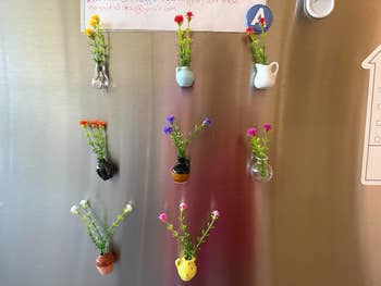 Small vases with flowers are magnetically attached to a metallic surface, arranged in a grid pattern