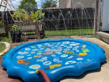 Inflatable splash pad with alphabet letters printed on it, spraying water in a backyard setting