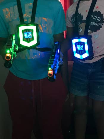 Reviewer showing two people wearing the glowing vests and holding lit up laser guns