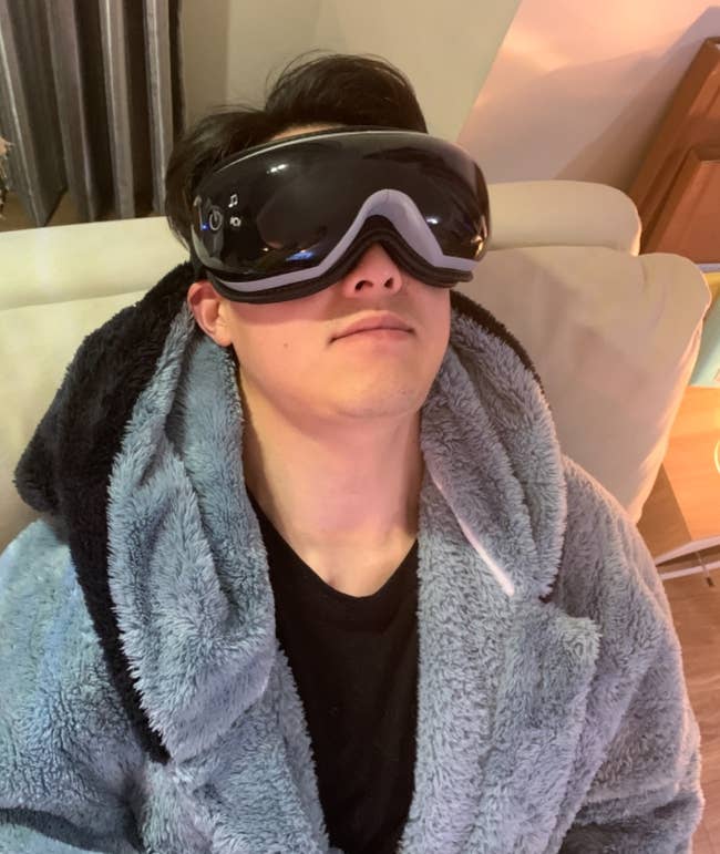 Person relaxing on a couch, wearing a plush robe and the Renpho Eye Massager