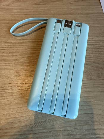 Portable power bank with integrated charging cables and USB ports on a wooden surface