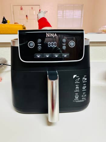 Ninja air fryer on a kitchen counter with control panel buttons for air fry, roast, reheat, and dehydrate, featuring a digital display
