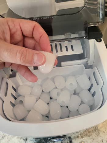 Hand holding an ice nugget over a full ice maker tray, showcasing its ice-making capacity