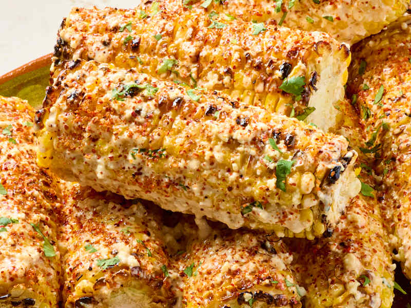 Grilled corn on the cob coated with creamy sauce, chili powder, and cilantro, arranged in a bowl.