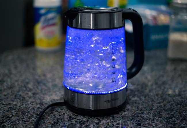 Electric kettle with water boiling, placed on a granite countertop, surrounded by household items