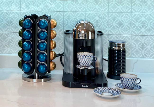 Espresso machine with coffee capsules arranged in a holder, accompanied by a patterned teacup set on a countertop