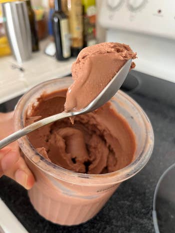 A spoonful of chocolate ice cream is being scooped from a container in a kitchen setting