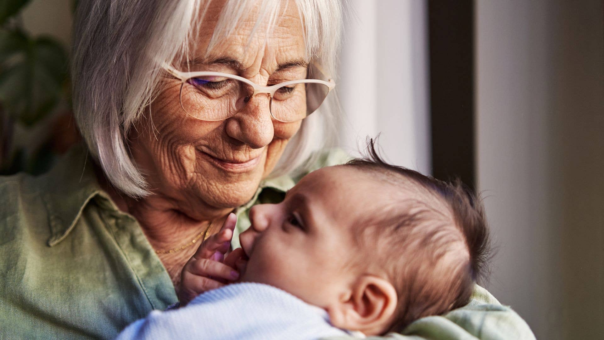 Close up portrait of a happy grandmother with gray hair holding her newborn grandchild