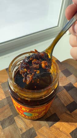 Jar of chili crisp on a wooden board, with a spoon scooping a portion