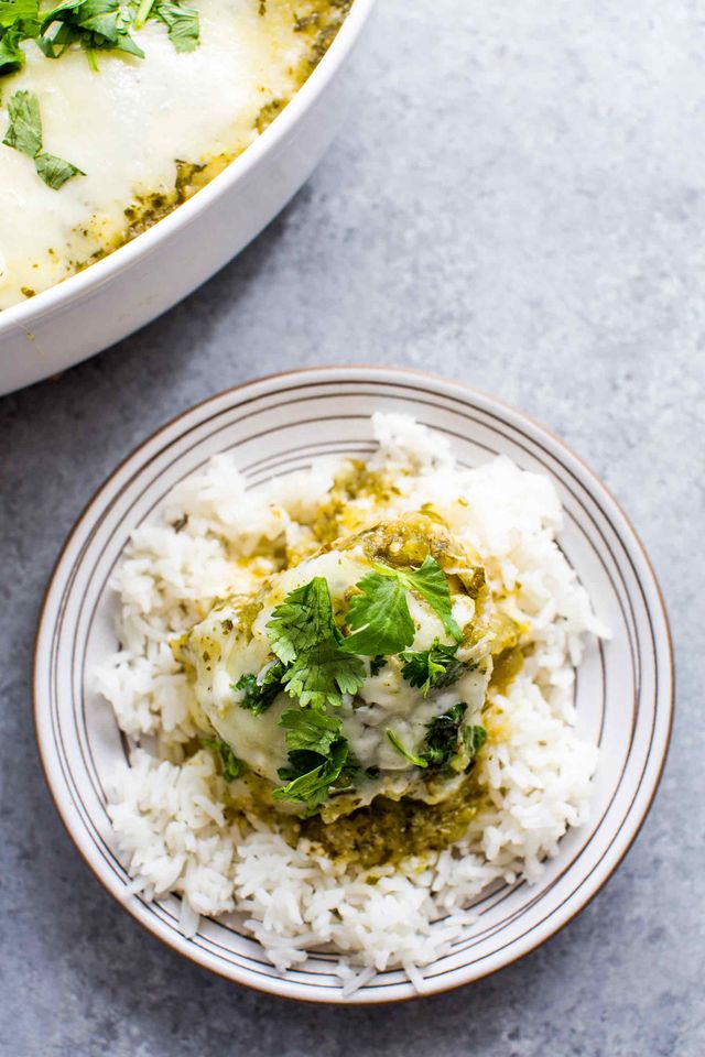 A serving of salsa verde chicken on a plate with rice garnished with cilantro with a casserole dish in the background