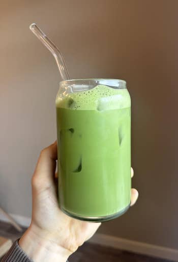 Person holding a glass of iced matcha latte with a clear straw