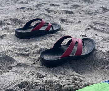 Sandals on a beach with people and umbrellas in the background, suggesting a casual day by the sea