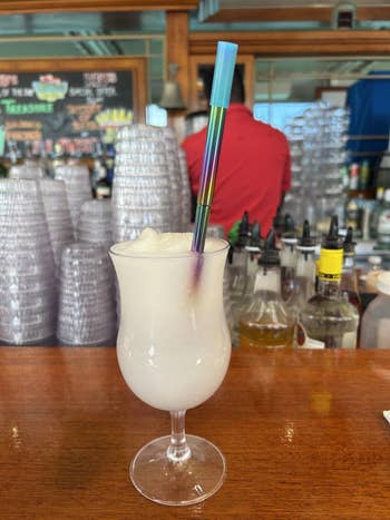 Frosty cocktail in a stemmed glass with a colorful straw, set on a bar counter with various drink mixers in the background