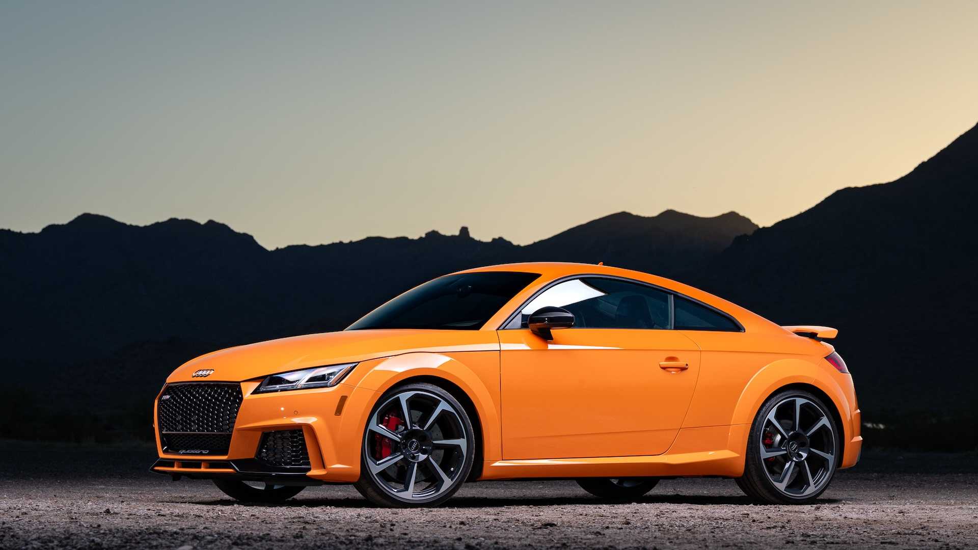 Front quarter of an orange Audi sports car parked in front of a mountain ridge