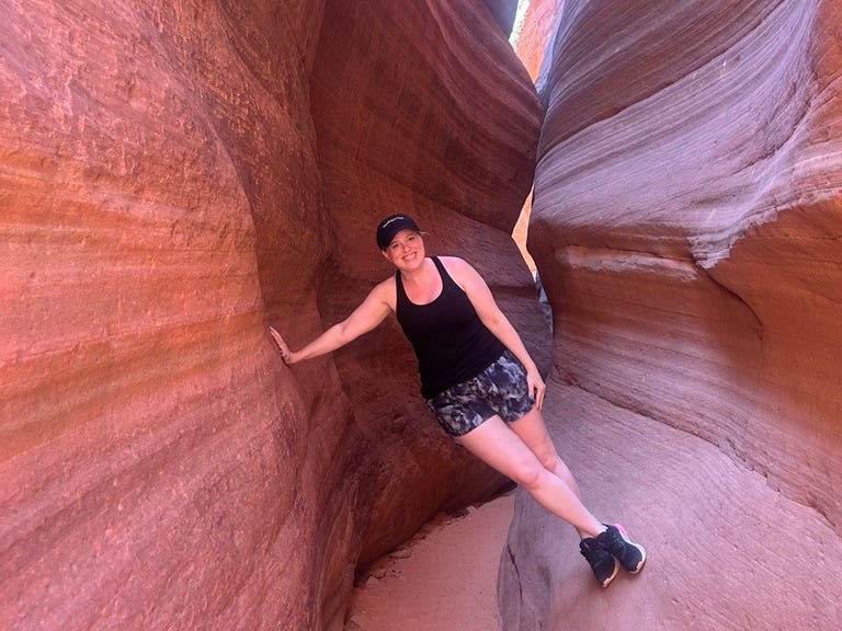 Woman leaning between narrow red rocks, smiling