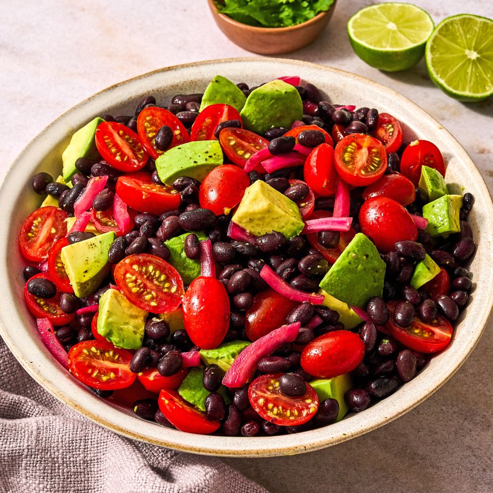 Bowl containing avocado black beans cherry tomatoes and red onions