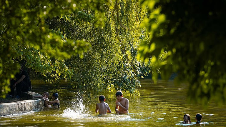 Unos jóvenes se bañan en un lago en un día tórrido, mientras el servicio meteorológico nacional emite alerta roja por calor extremo en parte del país, en Bucarest, Rumanía.