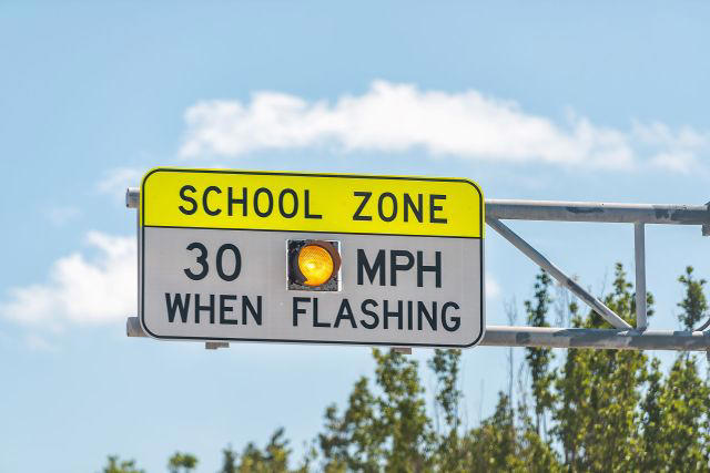 A traffic sign indicating a school zone with a speed limit of 30 MPH when the light is flashing.