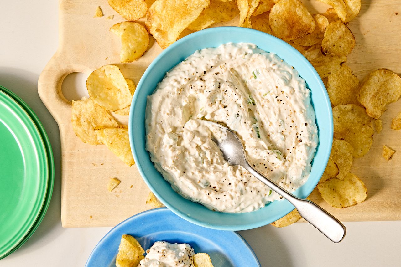 Bowl of dip garnished with black pepper next to potato chips on a cutting board