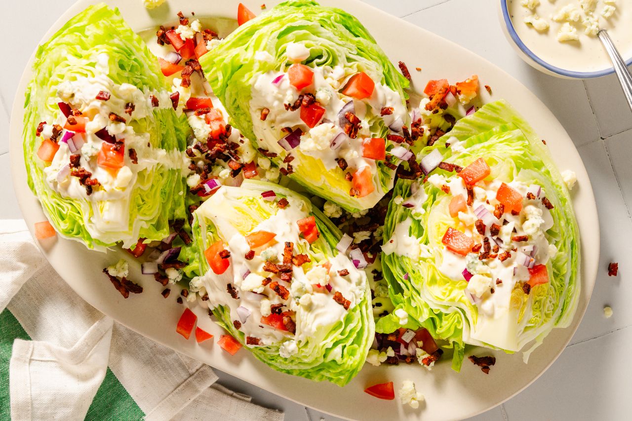 A platter of iceberg wedge salads topped with diced tomatoes red onions bacon bits and blue cheese dressing