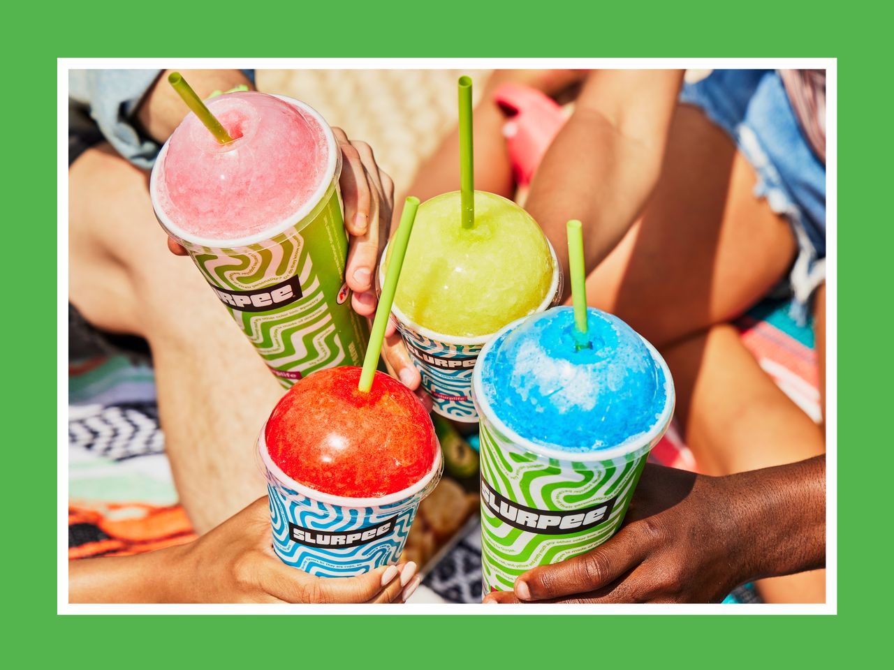 four hands holding together four slurpees from 7-eleven