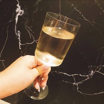 A hand holds a frosted wine glass against a marble background, suggesting a lifestyle or home decor theme