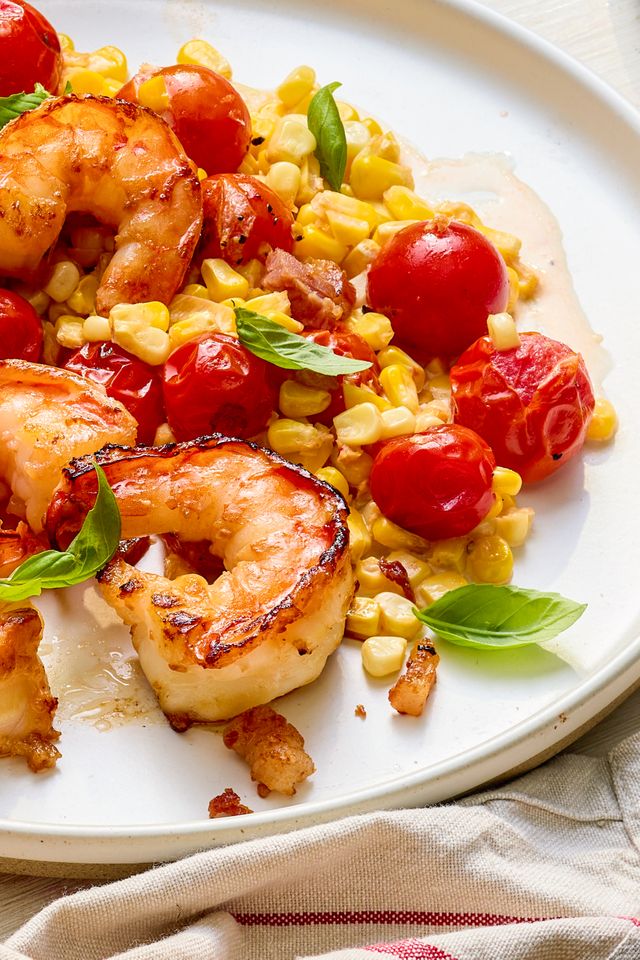 Close-up: plate of creamy skillet shrimp with corn, pancetta, and tomatoes on a white and red table napkin