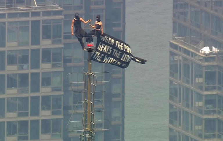 Two people climb on top of the Empire State Building with message on banner