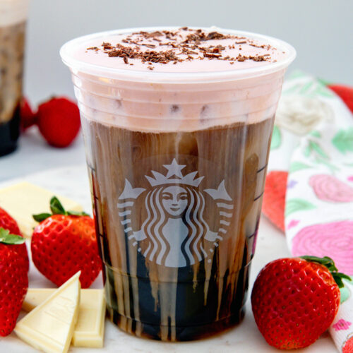 Closeup view of a White Chocolate Strawberry Cream Cold Brew in a Starbucks cup with chocolate shavings on top.
