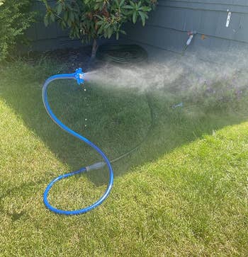 Garden hose with a spray nozzle attached, watering grass in a backyard setting near a house with siding