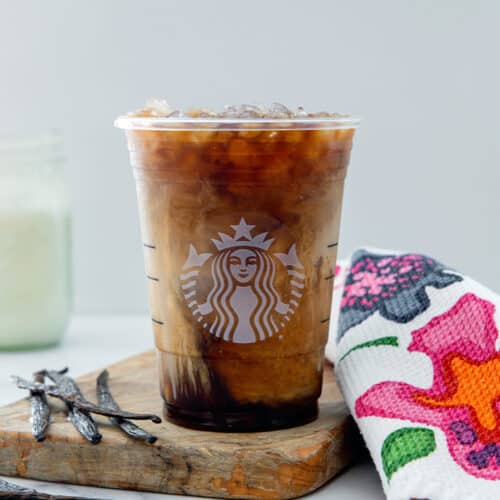 Head-on view of a Vanilla Sweet Cream Cold Brew with vanilla beans on side and jar of sweet cream in background.