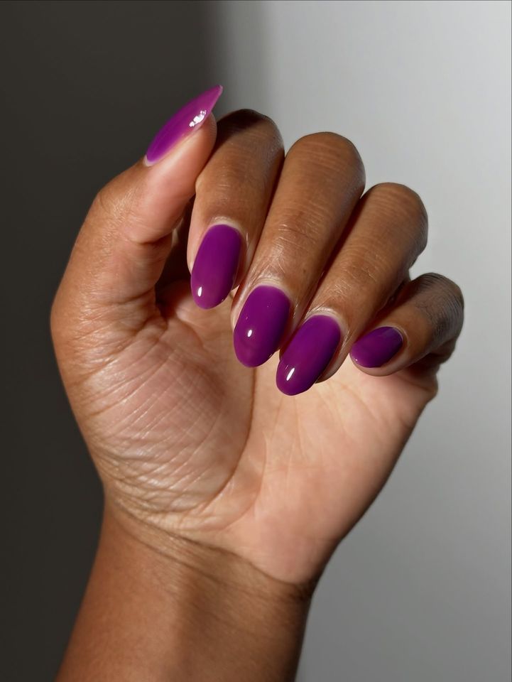 Closeup of a hand with nails painted purple shown against a neutral background