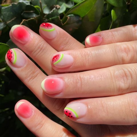 Closeup of nails with a watermelon design surrounded by greenery