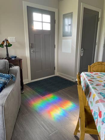 Sunlight casts a rainbow pattern on the floor in a cozy, decorated living room near the door, suggesting a tranquil, homey atmosphere