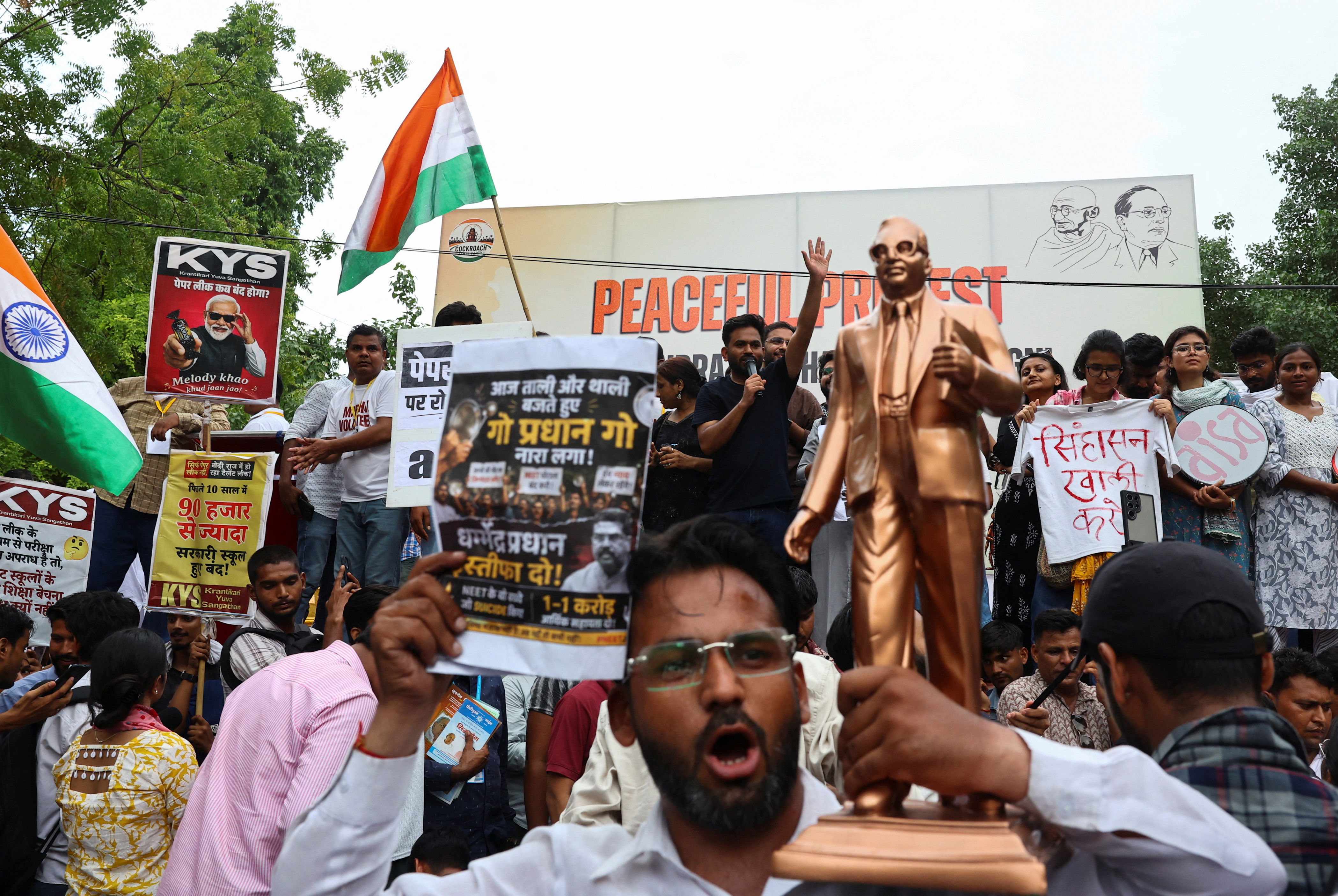 People hold placards and shout slogans as Abhijeet Dipke, head of the Cockroach Janta Party (CJP), waves to the crowd during a sit-in protest demanding the resignation of Indian education minister Dharmendra Pradhan (Reuters)