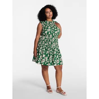 Person in sleeveless floral dress and sandals, posing confidently. The dress features a gathered waist and flowing skirt, ideal for casual outings